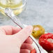 A person holding a Libbey stainless steel cocktail fork over a plate of vegetables.