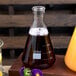 An American Metalcraft glass Erlenmeyer flask filled with brown liquid on a table.