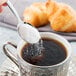 A Libbey stainless steel demitasse spoon pouring sugar into a cup of coffee.