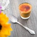 A Libbey Lady Astor stainless steel dessert spoon next to a glass of liquid on a table.