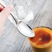 A hand holding a Libbey Lady Astor stainless steel dessert spoon over a glass of liquid.