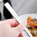 A hand holding a Libbey stainless steel dinner fork over a white plate of food.