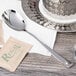 An Arcoroc stainless steel teaspoon on a saucer with a tea bag.