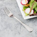 A Libbey stainless steel salad fork next to a plate of salad.