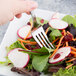 A hand holding a Libbey stainless steel salad fork over a vegetable salad.