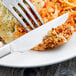 A Libbey stainless steel dinner knife and fork on a plate with food.