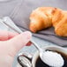 A hand holding a Libbey stainless steel demitasse spoon with sugar in it.