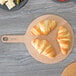 An Epicurean round pizza board with croissants on it on a table.