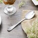 A Libbey medium weight stainless steel dessert spoon on a napkin next to a glass of dessert.