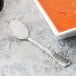 A Libbey medium weight stainless steel bouillon spoon next to a bowl of soup.