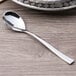 An Arcoroc stainless steel demitasse spoon with a silver handle on a table.