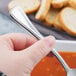 A person holding a Libbey stainless steel bouillon spoon in front of a bowl of soup.