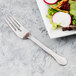 A Libbey stainless steel salad fork next to a plate of salad.