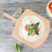 A pizza on an Epicurean wood pizza peel with tomatoes and basil on top.