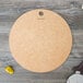 A round Epicurean natural wood fiber pizza board with a pizza cutter and pepper on a table.