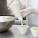 A person in white gloves holding a white bowl of green frosting and a pastry bag.