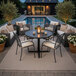 A 36-inch round black steel laminate outdoor or indoor standard height table with a cross base, set in a patio area.