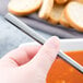 A person holding a Libbey stainless steel bouillon spoon in front of a bowl of soup.