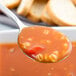 A Libbey stainless steel bouillon spoon holding soup over a blurred piece of bread.