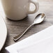 A Chef & Sommelier stainless steel demitasse spoon on a table next to a white mug.