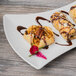 A Schonwald white porcelain bowtie tray holding three pastries with chocolate sauce and nuts.