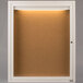 An Aarco white powder coated indoor bulletin board cabinet with a cork board inside.