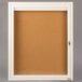 A white Aarco bulletin board cabinet with a frame and a door with a keyhole.