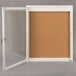 A white frame with a glass door covering a cork board.