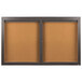A brown bulletin board with a black metal frame and two glass doors.