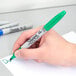 A hand holding a green Sharpie marker writing on a white surface.