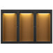 A black Aarco bulletin board cabinet with 3 glass doors and lights on a brown surface.