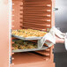 A person using a Cambro double compartment tray carrier to hold trays of food in an oven.