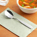 A Choice medium weight stainless steel bouillon spoon on a napkin next to a bowl of soup.