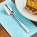 A Choice Bellwood stainless steel teaspoon on a napkin next to a slice of pumpkin pie.