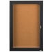 A black Aarco bulletin board cabinet with a cork board inside and a key lock.