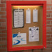 An Aarco red powder coated indoor bulletin board cabinet with 1 door.