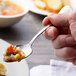 A person holding a Chef & Sommelier stainless steel teaspoon full of food.