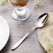 A Chef & Sommelier Lazzo stainless steel dessert spoon on a table next to a glass of milk.