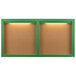 A green framed bulletin board with 2 doors and lights on the wall.