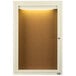 An ivory enclosed bulletin board cabinet with a light on it.