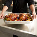 A person holding a Vollrath Wear-Ever roasting pan with cooked chicken and vegetables.