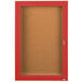 A red framed Aarco bulletin board cabinet with a hinged locking door.