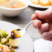 A person holding a Chef & Sommelier stainless steel teaspoon with food on it.