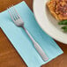 A Choice stainless steel dinner fork on a napkin next to a plate of food.