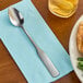 A Choice stainless steel medium weight iced tea spoon on a napkin.