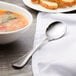 A Chef & Sommelier stainless steel soup spoon next to a bowl of soup.