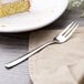 An Arcoroc stainless steel cake fork on a napkin with a piece of cake.