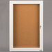 A white cabinet with a cork board inside and a glass door with a key.