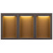 An Aarco bronze anodized indoor bulletin board cabinet with three glass doors and lights.