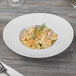 A Schonwald white porcelain bowl filled with pasta and a fork on a table.